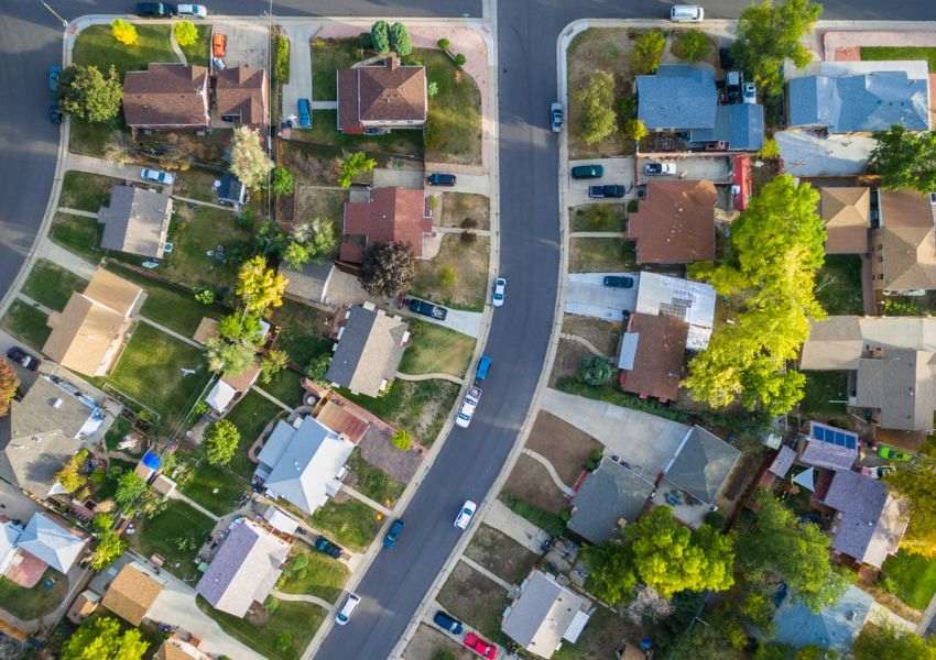 Bird’s eye view of a Denton County neighborhood is pictures, with single family homes lining a dark gray road with parked cars and patches of grass.
